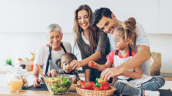 Family in kitchen smiling making a healthy salad.