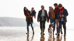 Multi-generational family with their dog walking on the beach.