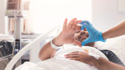 Patient in hospital bed making heart shape with his hands.