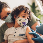 Child wearing a mask receiving a vaccination