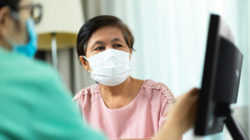 Woman wearing mask watches doctor pointing at medical history