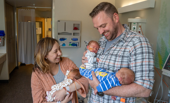 Parents holding three babies in NICU